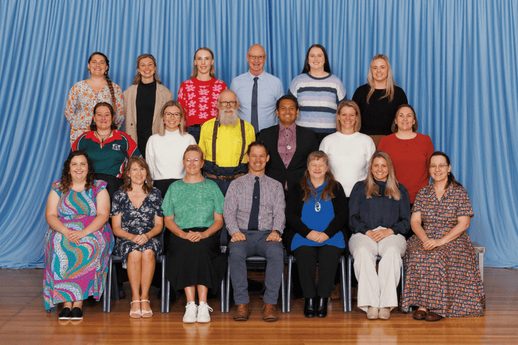 Group staff photo. Three rows of staff with a variety of colours in their clothing, blue curtain background.