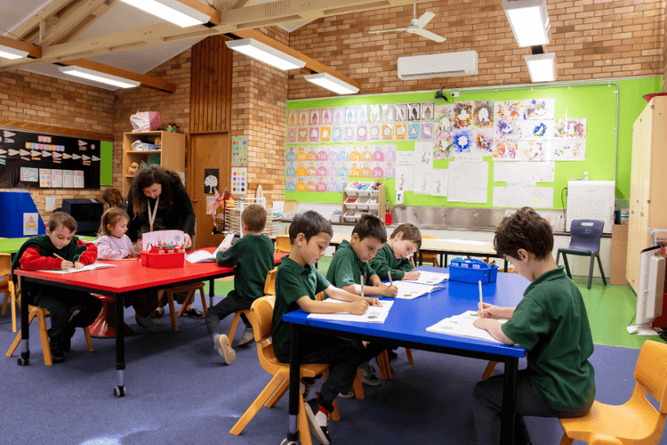 Kindergarten classroom, with bright colourful artwork and 7 students working at their desk with their teacher's support.