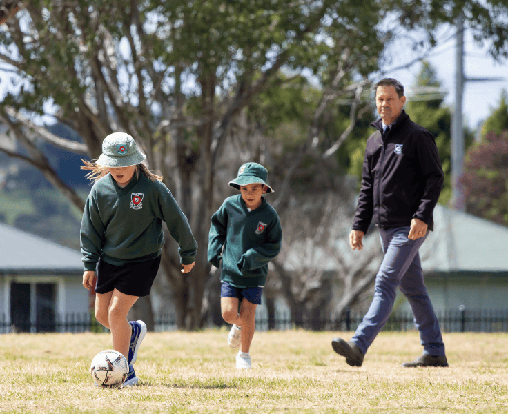 The principal and two students playing soccer on our oval.